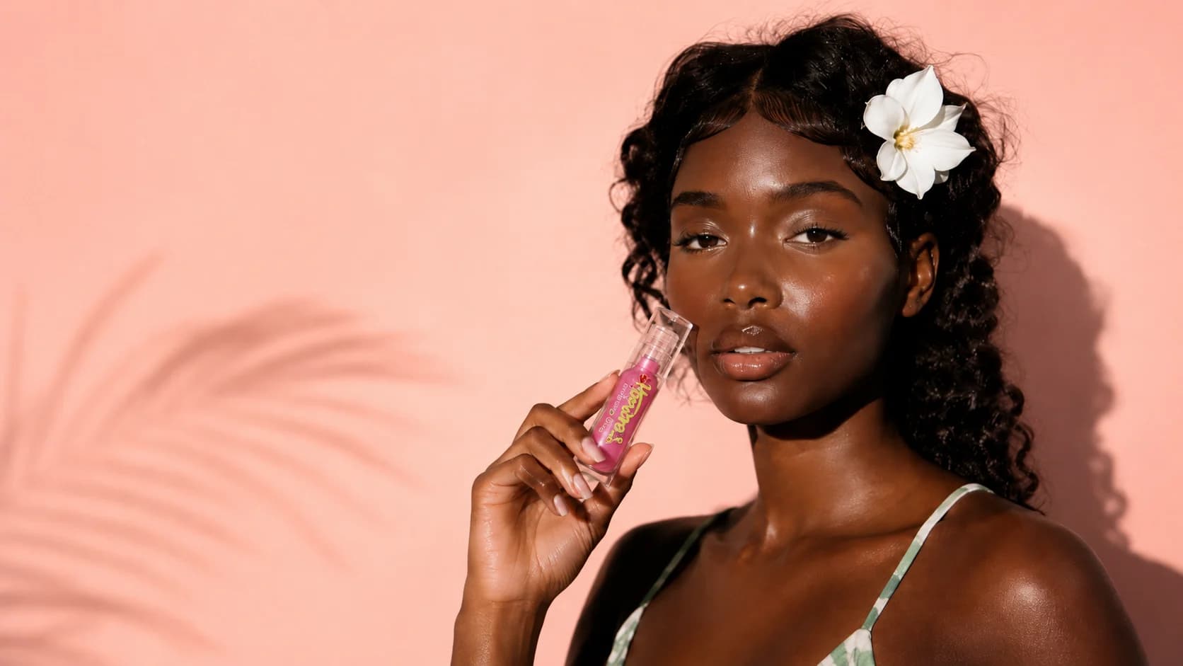Honora's lip gloss held beside a model against a warm peach campaign backdrop